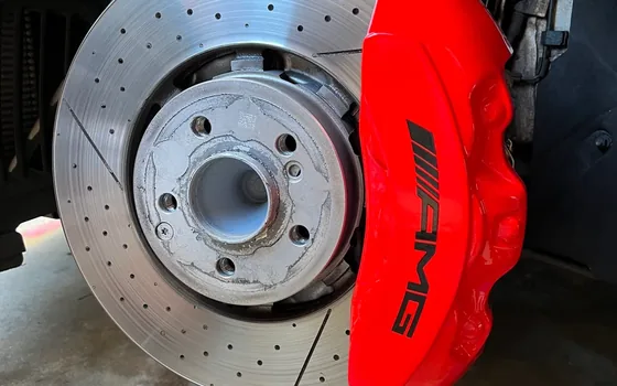 Red Mercedes-AMG brake caliper over a drilled brake rotor
