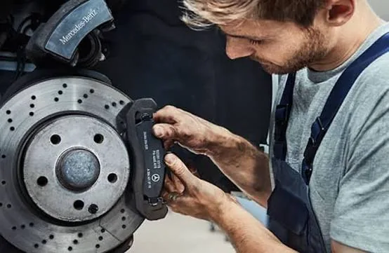 Technician installing a new brake pad on a Mercedes-Benz drilled rotor